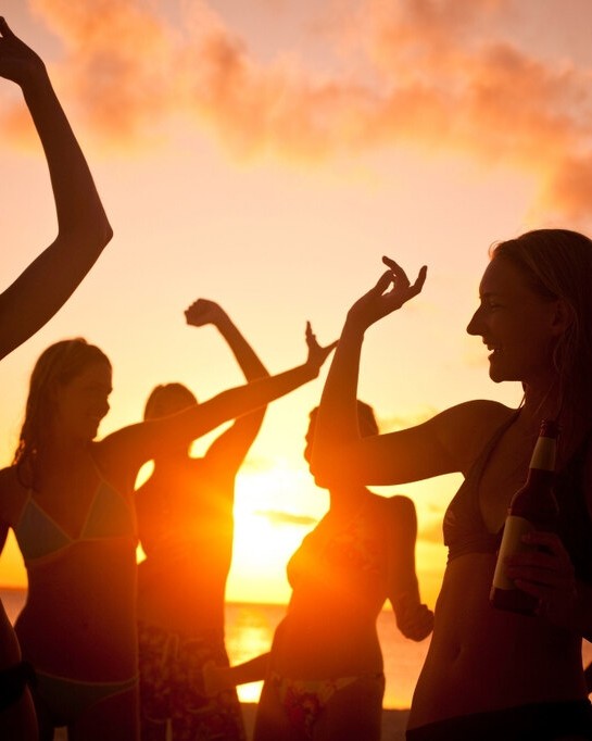 Mulheres curtindo sunset party à beira-mar ao pôr do sol com look para festa na praia leve e confortável