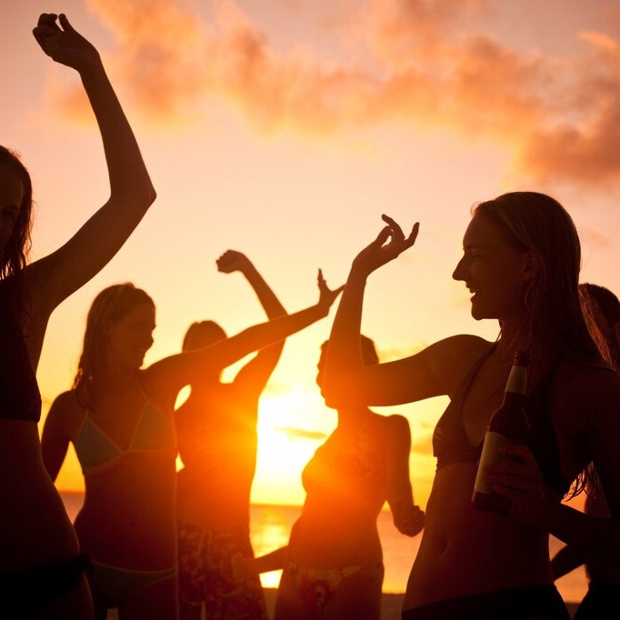 Mulheres curtindo sunset party à beira-mar ao pôr do sol com look para festa na praia leve e confortável