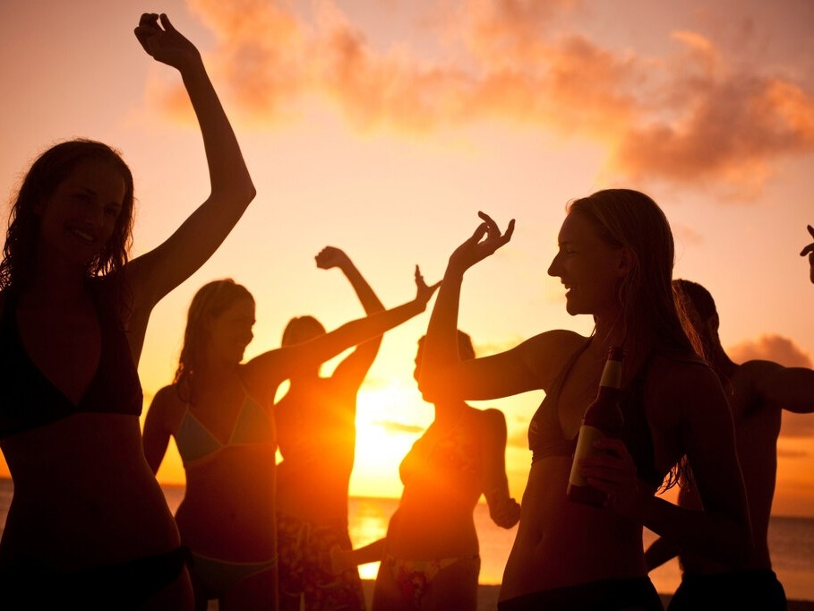 Mulheres curtindo sunset party à beira-mar ao pôr do sol com look para festa na praia leve e confortável