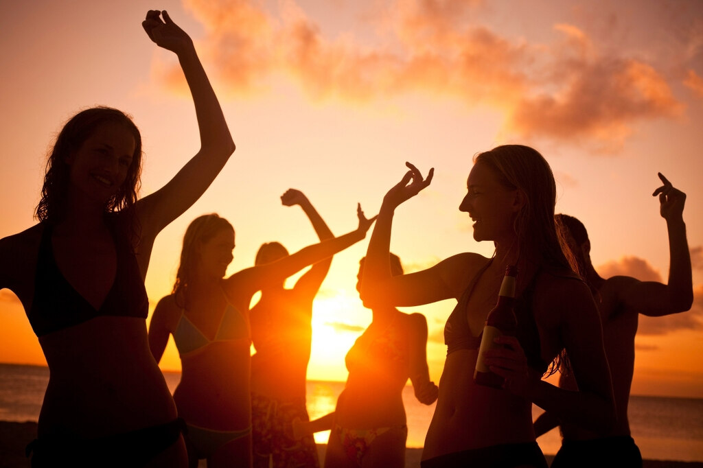 Mulheres curtindo sunset party à beira-mar ao pôr do sol com look para festa na praia leve e confortável