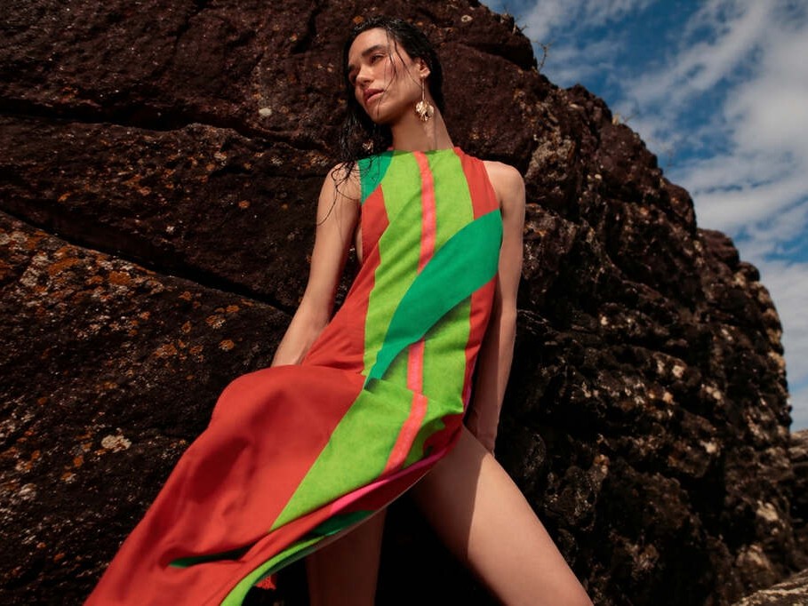 Mulher usando vestido leve estampado De Chelles encostada em pedra e com céu azul ao fundo, representando como usar saída de praia